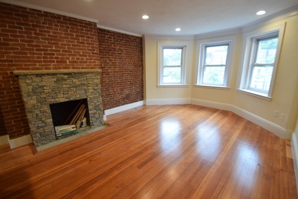 an empty room with wooden floor fireplace and windows