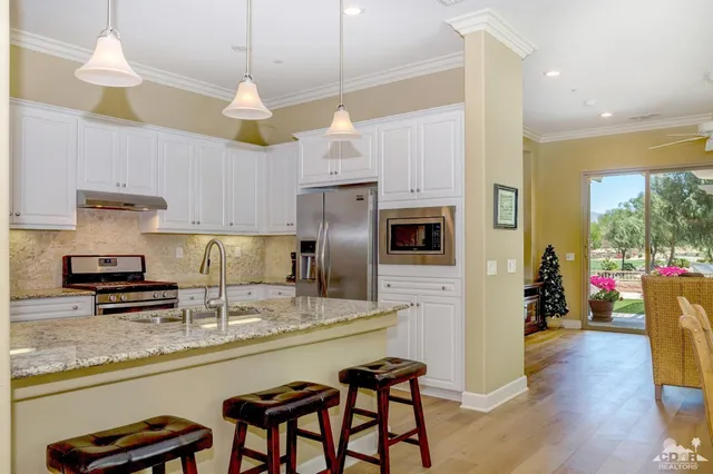 a kitchen with stainless steel appliances granite countertop a refrigerator a sink dishwasher a stove and a dining table with wooden floor