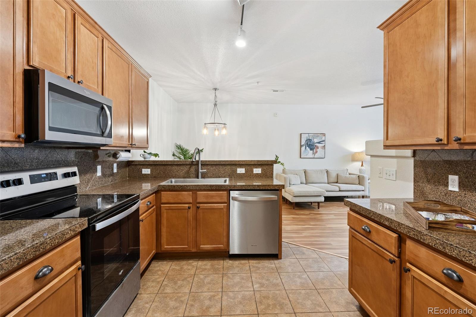 7140 Simms Street, Unit 102 Arvada, CO 80004 - Photo 8 of 34 a kitchen with stainless steel appliances granite countertop a stove a sink dishwasher and a microwave oven with large wooden cabinets