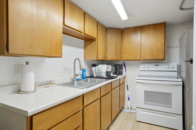 707 East 150 South Provo, UT 84606 - Photo 19 of 31 Kitchen featuring wood cabinetry, light-toned countertops, a stainless steel double basin sink with a high-arch faucet, a white electric range, and light wood-finish flooring