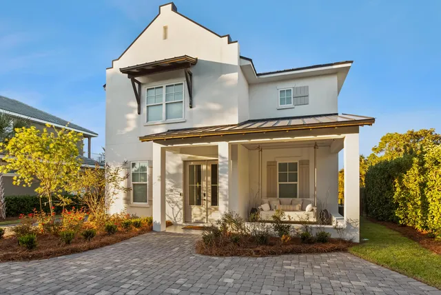 a view of a white house with large windows and a table and chairs in a patio