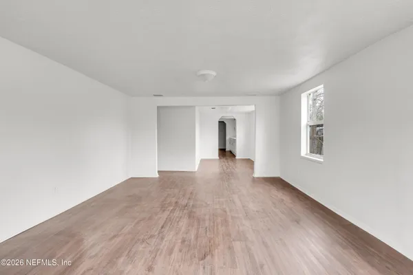 a view of an empty room with wooden floor and a window