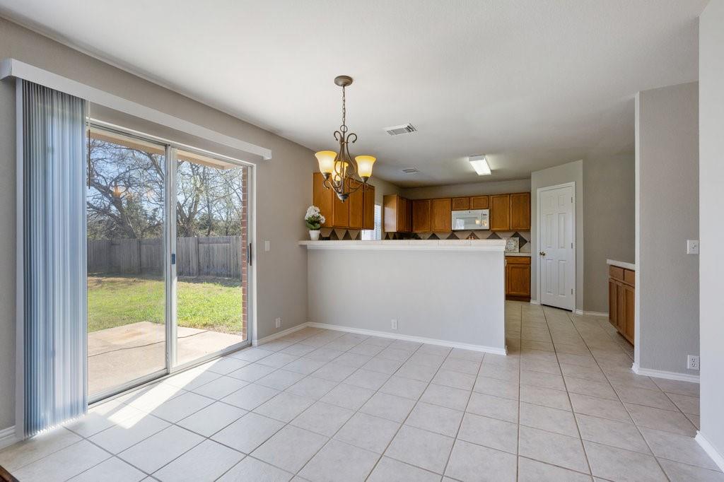 1216 Mathias Street Cedar Park, TX 78613 - Photo 5 of 16 Kitchen with brown cabinets, a chandelier, hanging light fixtures, a peninsula, and white microwave