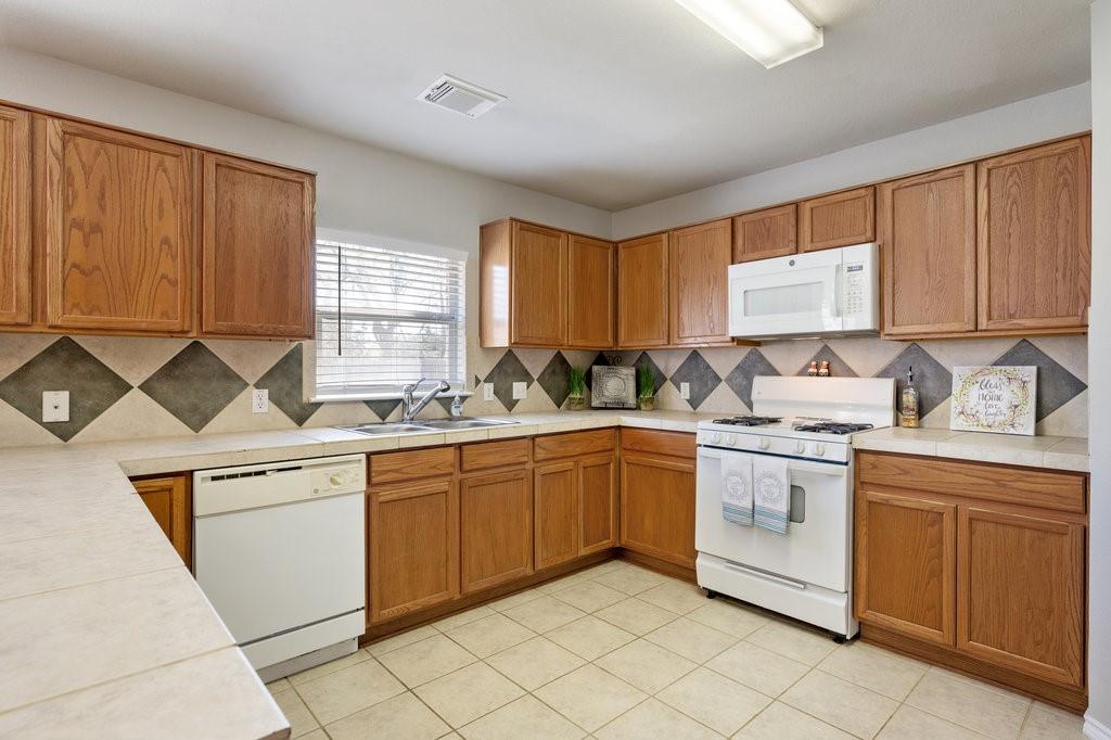 1216 Mathias Street Cedar Park, TX 78613 - Photo 6 of 16 Kitchen with white appliances, brown cabinetry, tasteful backsplash, and light tile patterned flooring