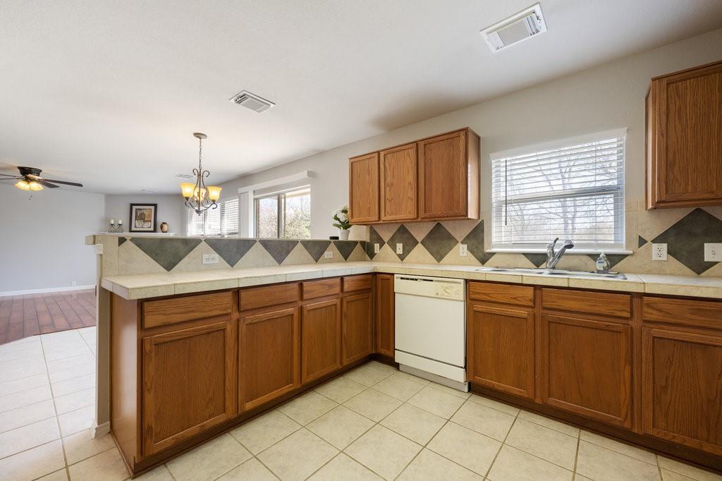 1216 Mathias Street Cedar Park, TX 78613 - Photo 7 of 16 Kitchen featuring brown cabinets, a peninsula, dishwasher, pendant lighting, and decorative backsplash