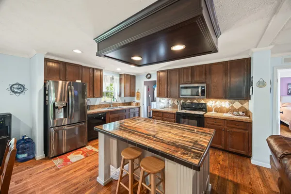a kitchen with stainless steel appliances kitchen island granite countertop a dining table chairs and wooden floor