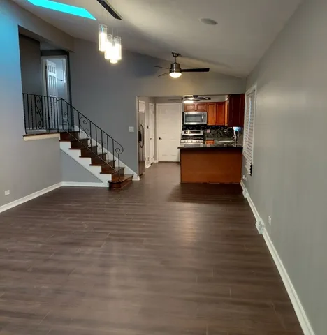 a view of an empty room with kitchen and stairs