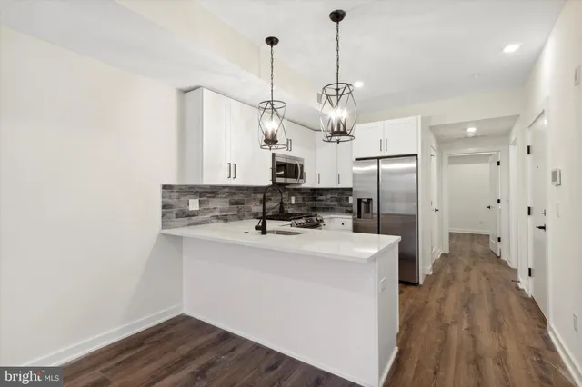 a kitchen with stainless steel appliances a refrigerator a sink dishwasher a stove and white cabinets with wooden floor