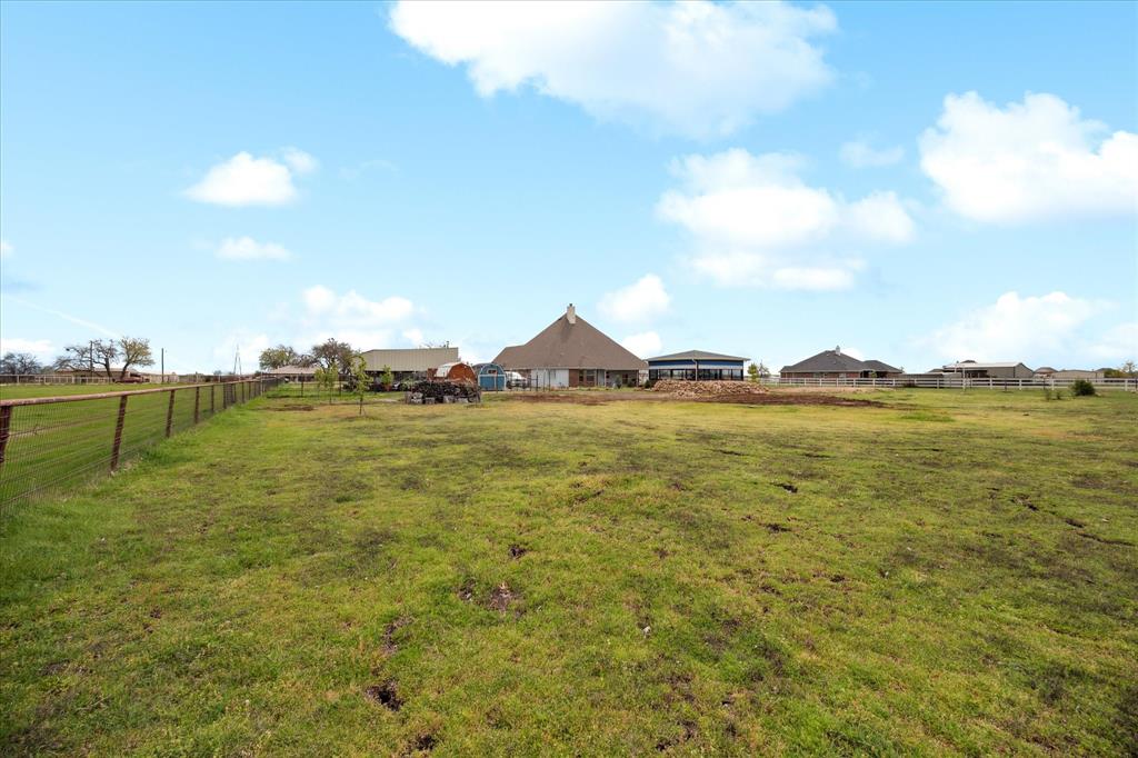 119 George Owens Road Ponder, TX 76259 - Photo 23 of 26 Expansive green acreage with perimeter fencing, featuring several single-story structures with varied rooflines in the background