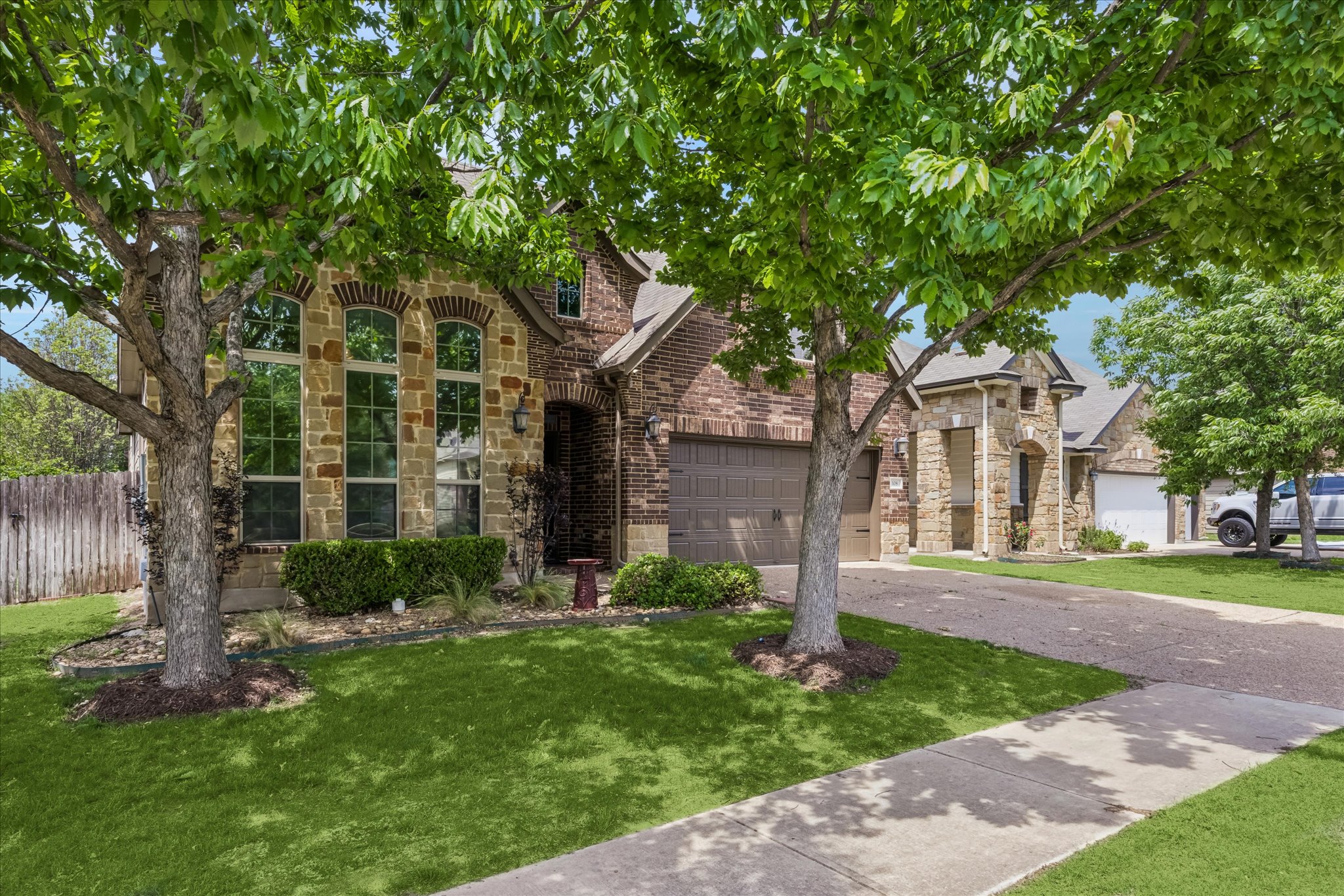 Stone and brick exterior featuring arched windows, an attached garage, a paved driveway, and a concrete sidewalk