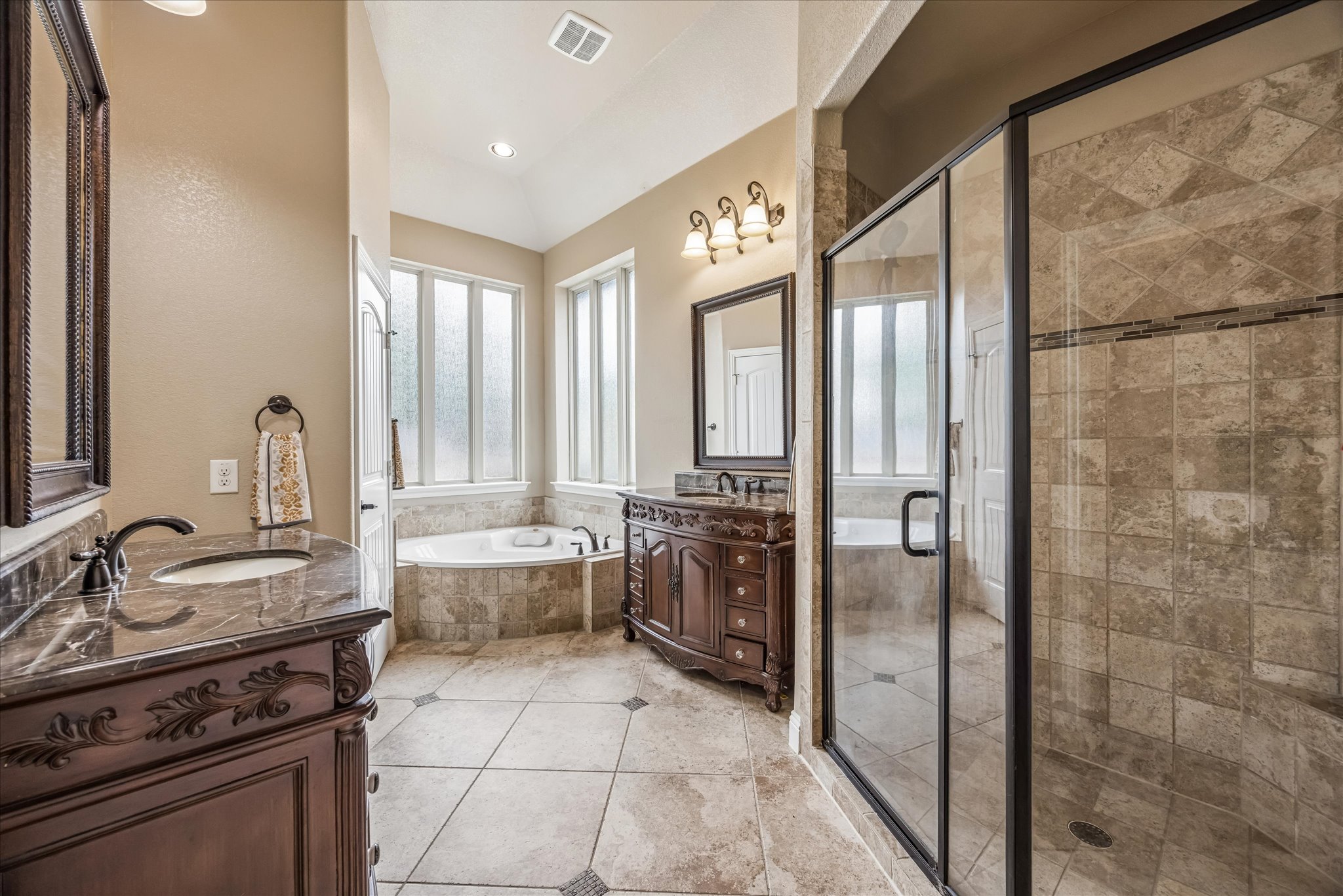 108 Rhinestone Cove Liberty Hill, TX 78642 - Photo 18 of 32 Spacious bathroom featuring a corner soaking tub, a frameless glass shower enclosure, and two dark wood vanities with undermount sinks and dark stone countertops