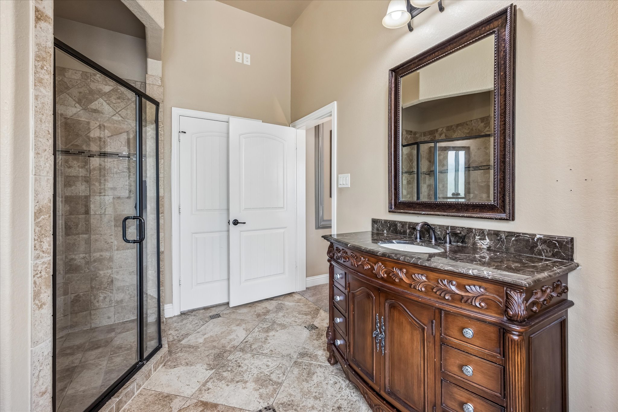 108 Rhinestone Cove Liberty Hill, TX 78642 - Photo 19 of 32 Spacious bathroom featuring a glass-enclosed shower with tiled walls, an ornate wood-finish vanity with a stone countertop, a framed mirror, and tiled flooring