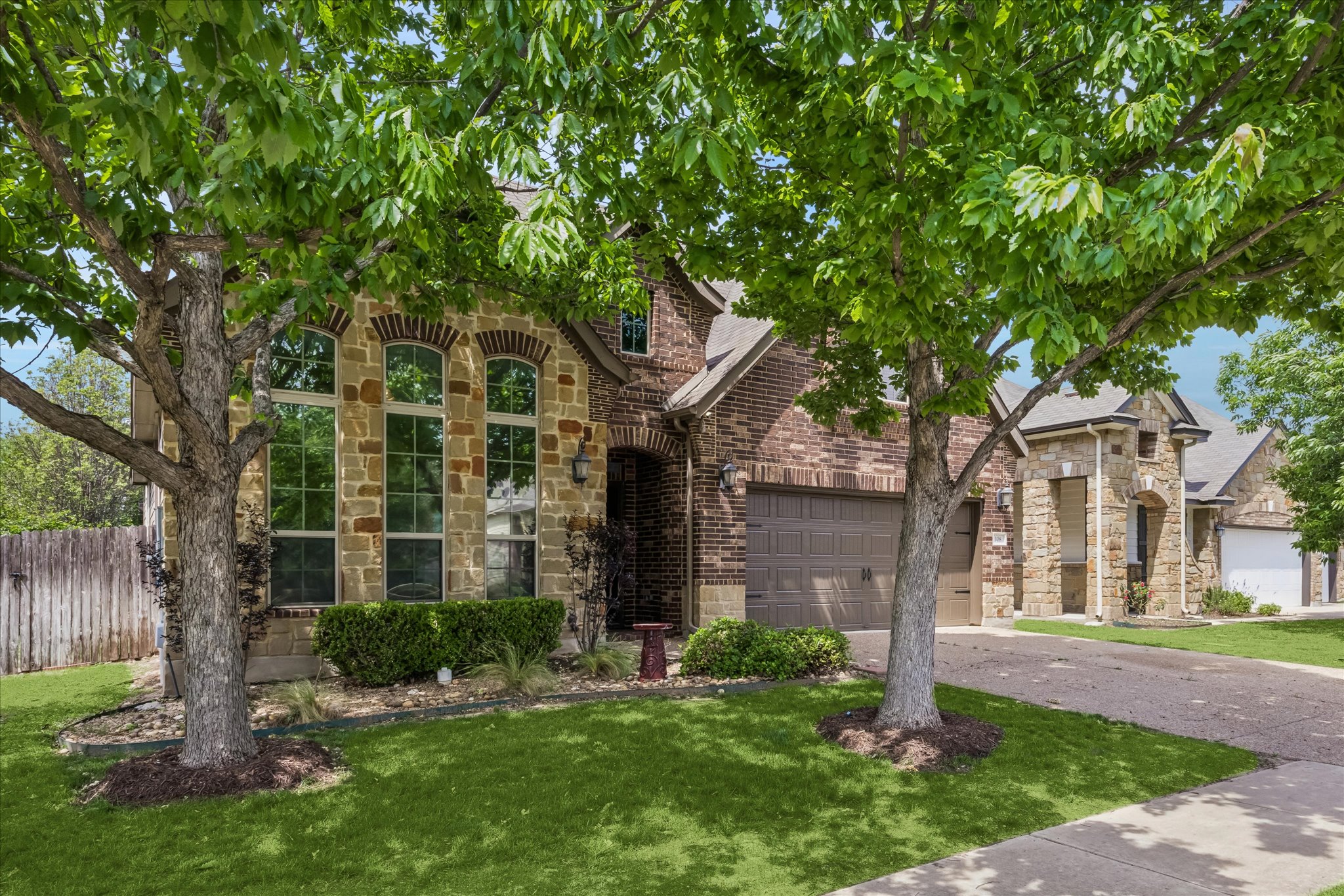 108 Rhinestone Cove Liberty Hill, TX 78642 - Photo 2 of 32 Brick and stone exterior featuring arched windows, an attached garage, a manicured lawn, and mature trees