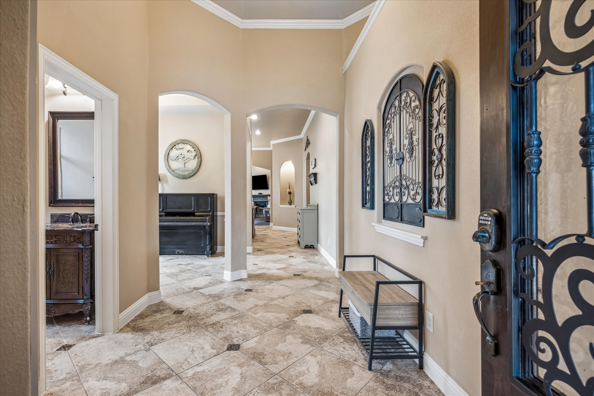 108 Rhinestone Cove Liberty Hill, TX 78642 - Photo 4 of 32 Spacious entry hallway featuring tile flooring with dark accent inlays, arched doorways, crown molding, and a decorative front door with wrought iron details