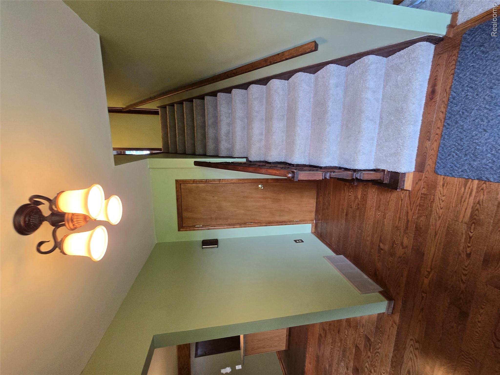 5282 McIntyre Road North Street, MI 48049 - Photo 35 of 53 Hardwood flooring, carpeted staircase, wood banister, wood-panel door, and a multi-bulb ceiling light fixture