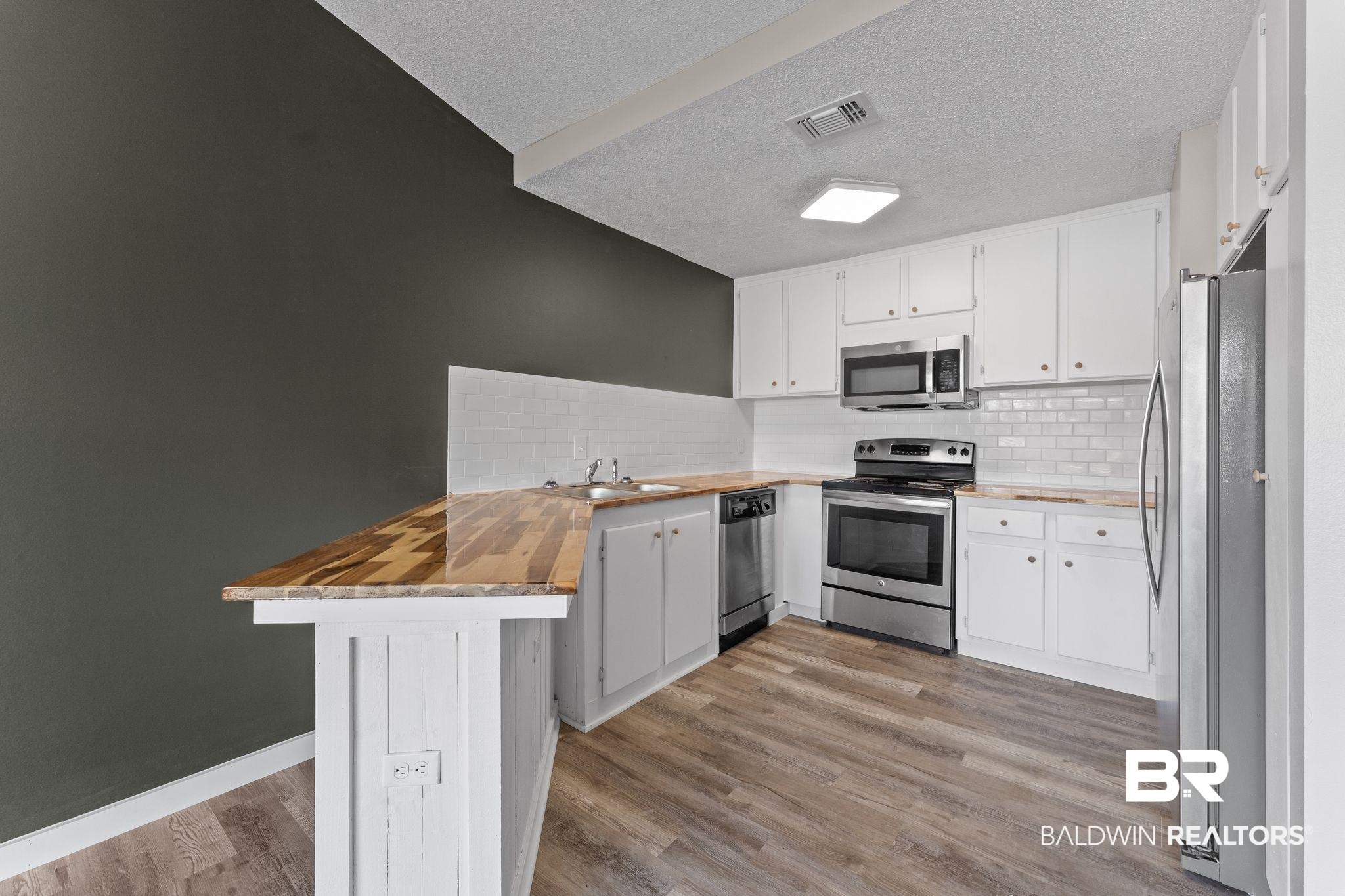 128 West Satsuma Avenue, Unit 128 Foley, AL 36535 - Photo 10 of 41 Kitchen with a peninsula, stainless steel appliances, butcher block countertops, white cabinets, and light wood-style flooring