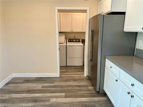 a view of a refrigerator in kitchen and an empty room with wooden floor