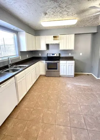 a large kitchen with granite countertop a stove a sink a counter space and cabinets