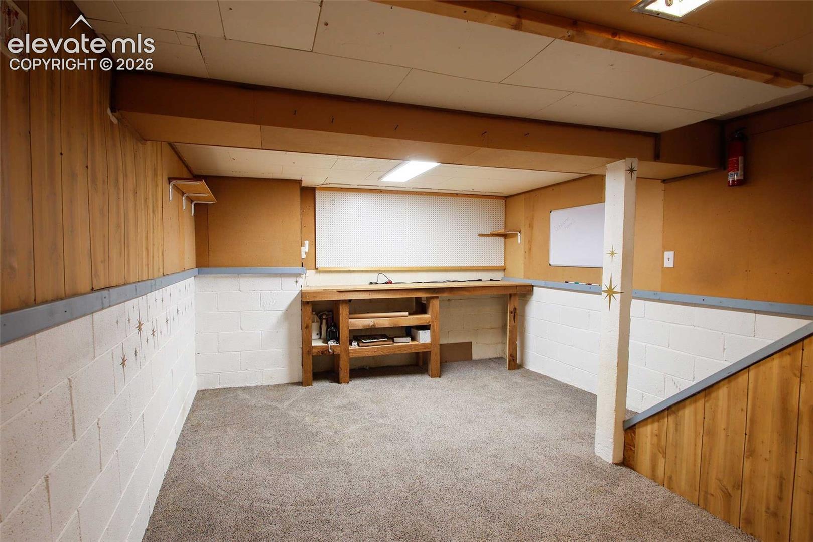 702 Erie Road Colorado Springs, CO 80910 - Photo 17 of 19 Carpeted area with exposed wood ceiling beams, white painted block walls, wood paneling, and a built-in wood workbench