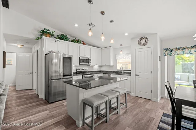 a kitchen with kitchen island a refrigerator a stove a sink and white cabinets with wooden floor