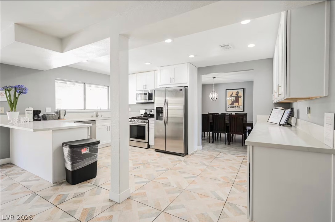 1803 Nuevo Road Henderson, NV 89014 - Photo 11 of 71 Kitchen with stainless steel appliances, white cabinets, a peninsula, light stone countertops, and hanging light fixtures