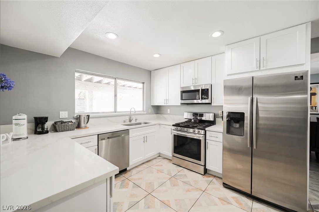 1803 Nuevo Road Henderson, NV 89014 - Photo 12 of 71 Kitchen featuring stainless steel appliances, white cabinets, light tile patterned floors, recessed lighting, and a peninsula