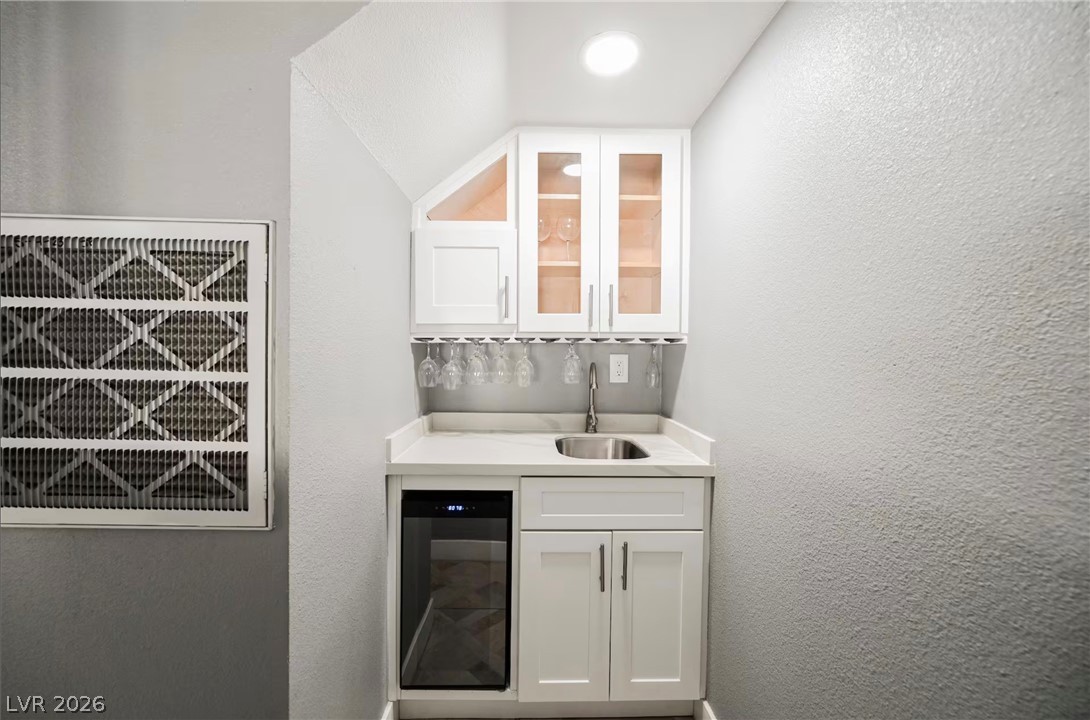 1803 Nuevo Road Henderson, NV 89014 - Photo 70 of 71 Indoor wet bar featuring white cabinetry, a textured wall, wine cooler, glass fronted cabinets, and light stone countertops