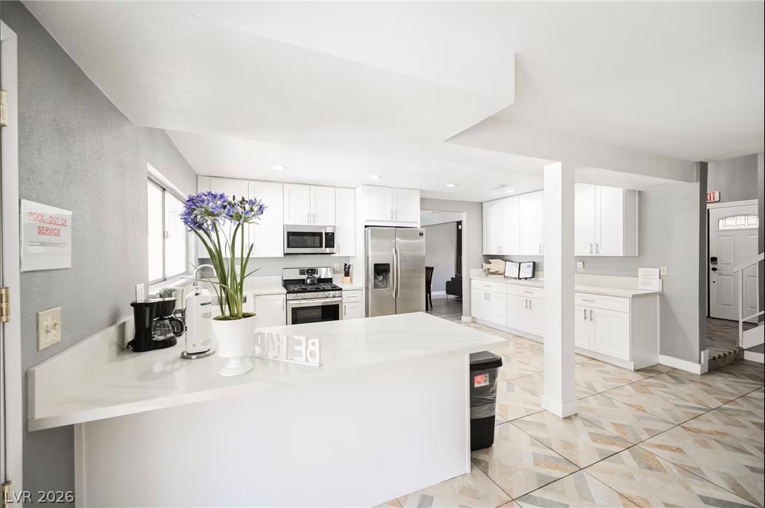 1803 Nuevo Road Henderson, NV 89014 - Photo 9 of 71 Kitchen with stainless steel appliances, a peninsula, white cabinets, and light stone counters