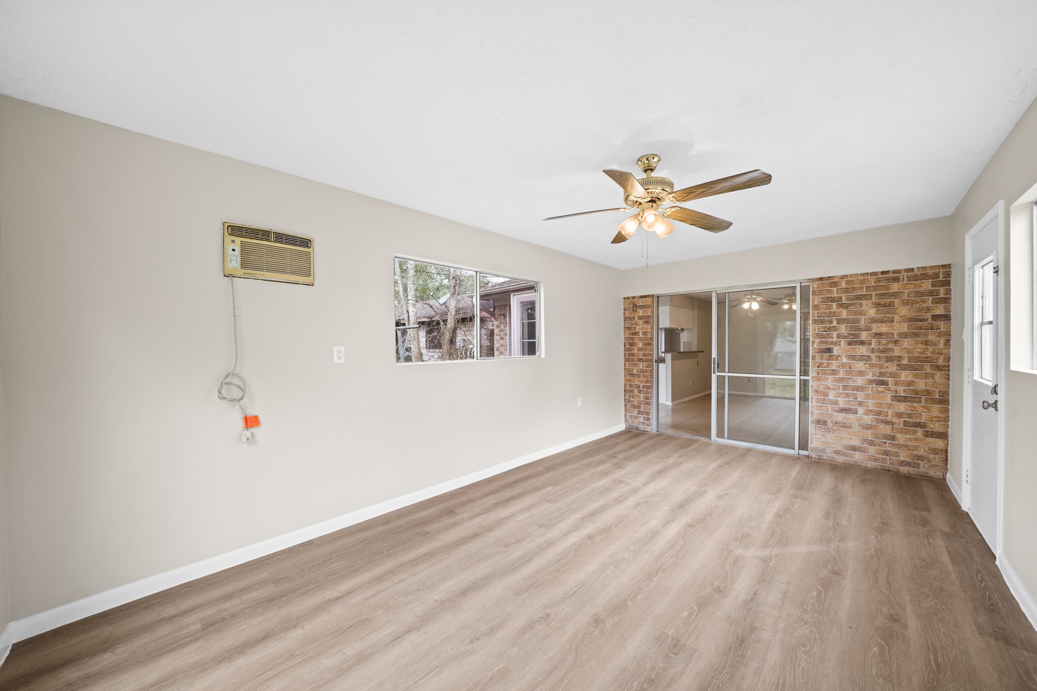 304 Cypress Street Alvin, TX 77511 - Photo 11 of 23 Spacious bonus room with wood-look flooring, ceiling fan, brick accent wall, and sliding glass doors connecting to the main living space.