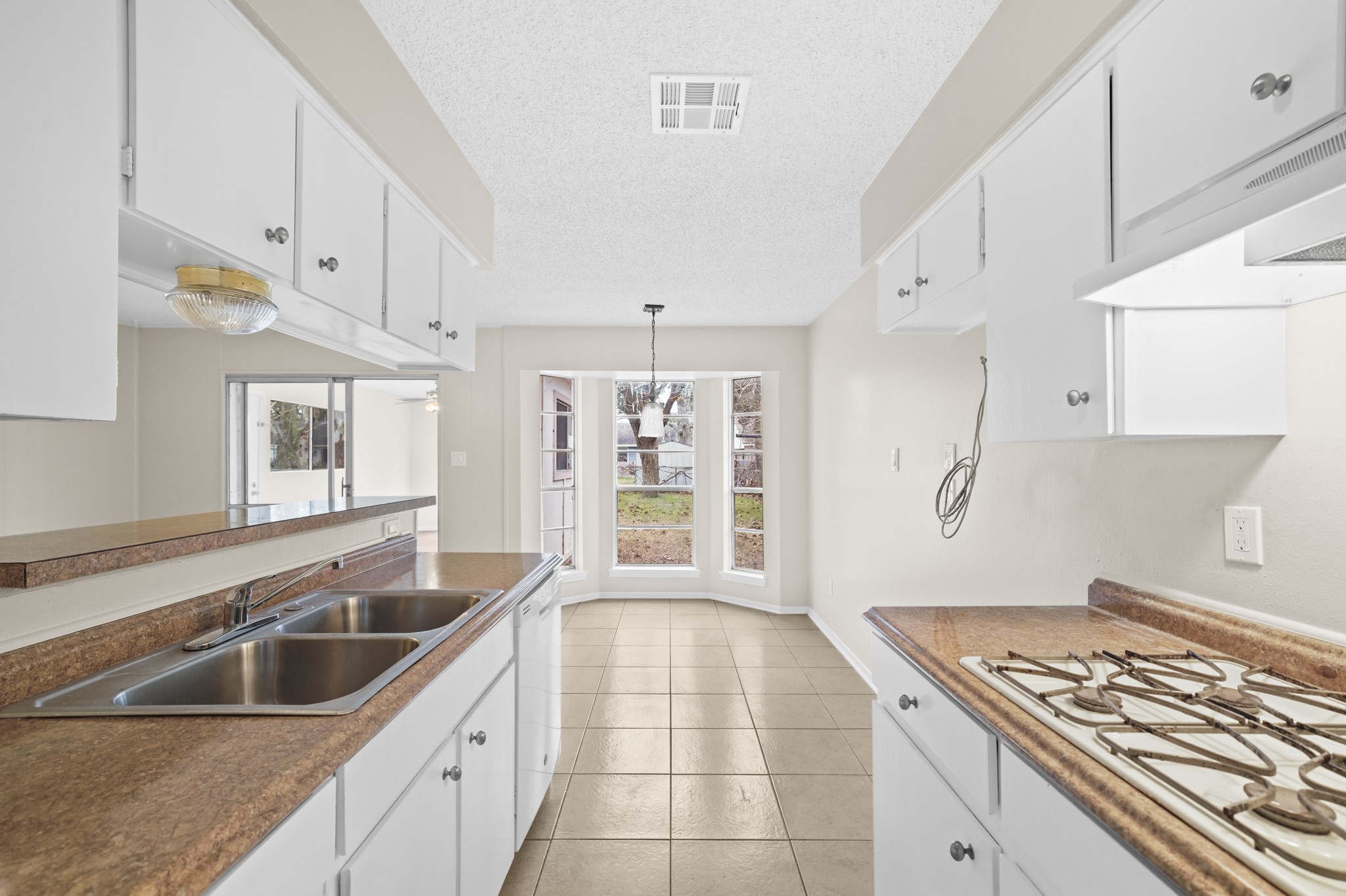 304 Cypress Street Alvin, TX 77511 - Photo 15 of 23 Bright galley-style kitchen with tile flooring, white cabinetry, ample counter space, and a view into the breakfast area with bay window.