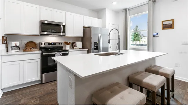 a kitchen with stainless steel appliances granite countertop a sink a stove a refrigerator cabinets and chairs with wooden floor