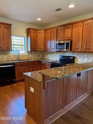 a kitchen with stainless steel appliances granite countertop wooden cabinets a stove top oven a sink and dishwasher with wooden floor