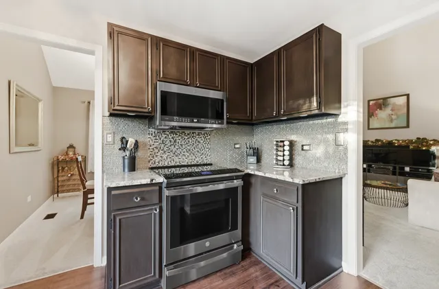 a kitchen with stainless steel appliances granite countertop a stove top oven a sink dishwasher a dining table and chairs with wooden floor