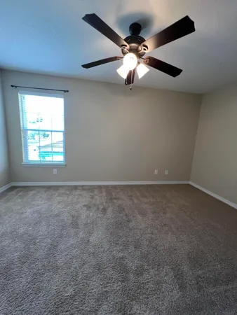 an empty room with chandelier fan and windows