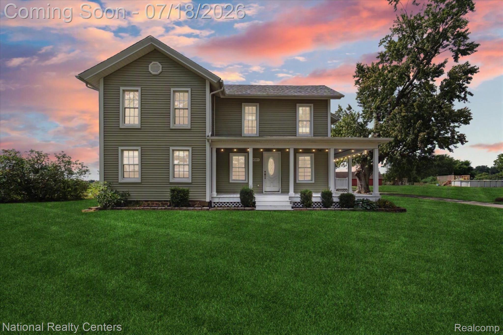 Two-story residence featuring sage green siding, white trim, a covered front porch, a gabled roofline, and a prominent front lawn