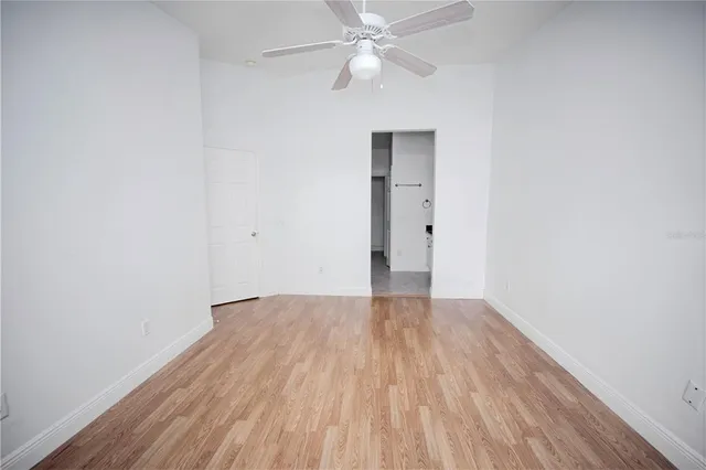 a view of an empty room with wooden floor and a ceiling fan