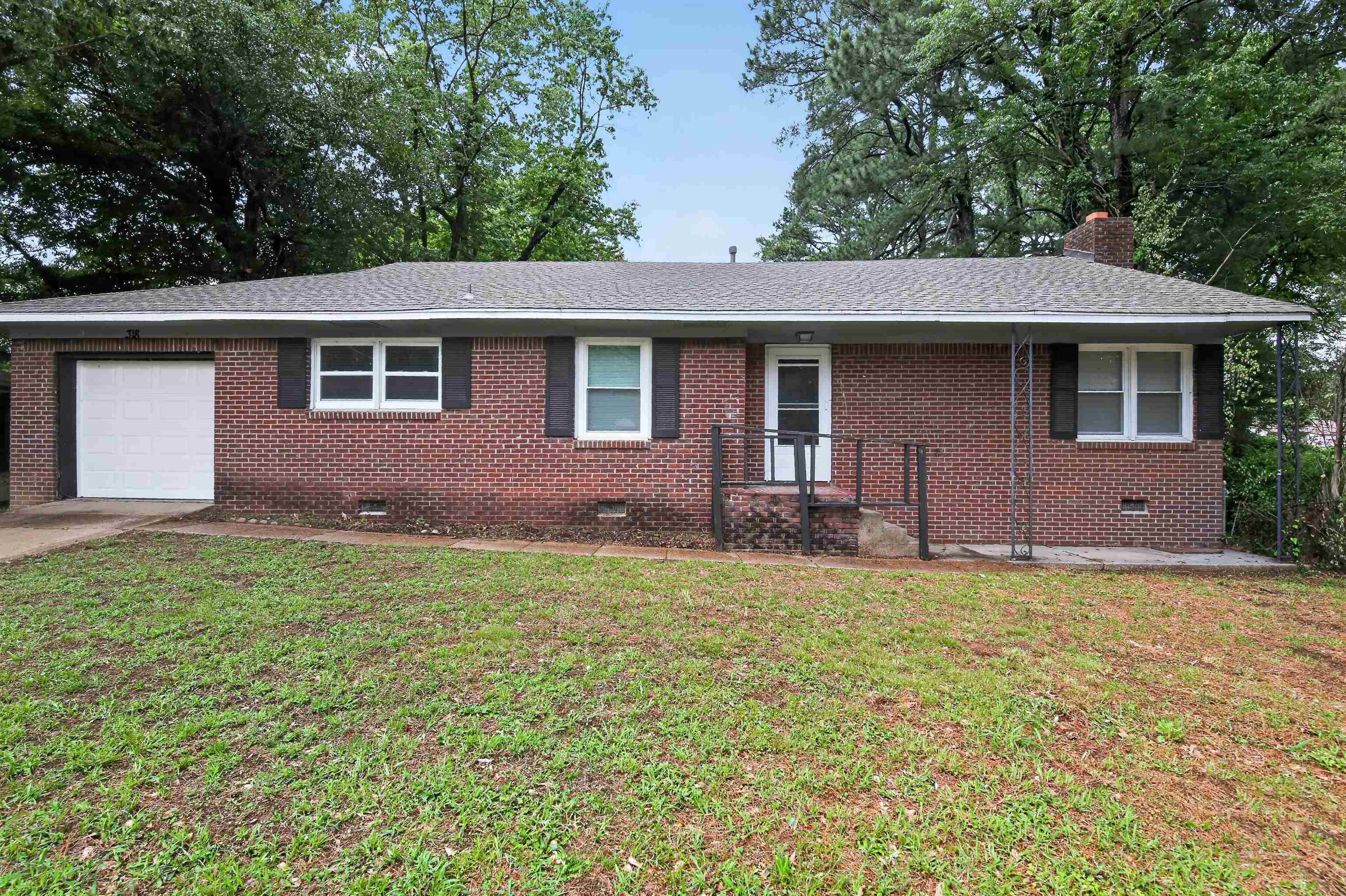 318 East Raines Road Memphis, TN 38109 - Photo 7 of 28 Brick exterior home featuring an attached garage with a white door, a covered front porch with metal railings, a shingled roof, and multiple windows with dark shutters