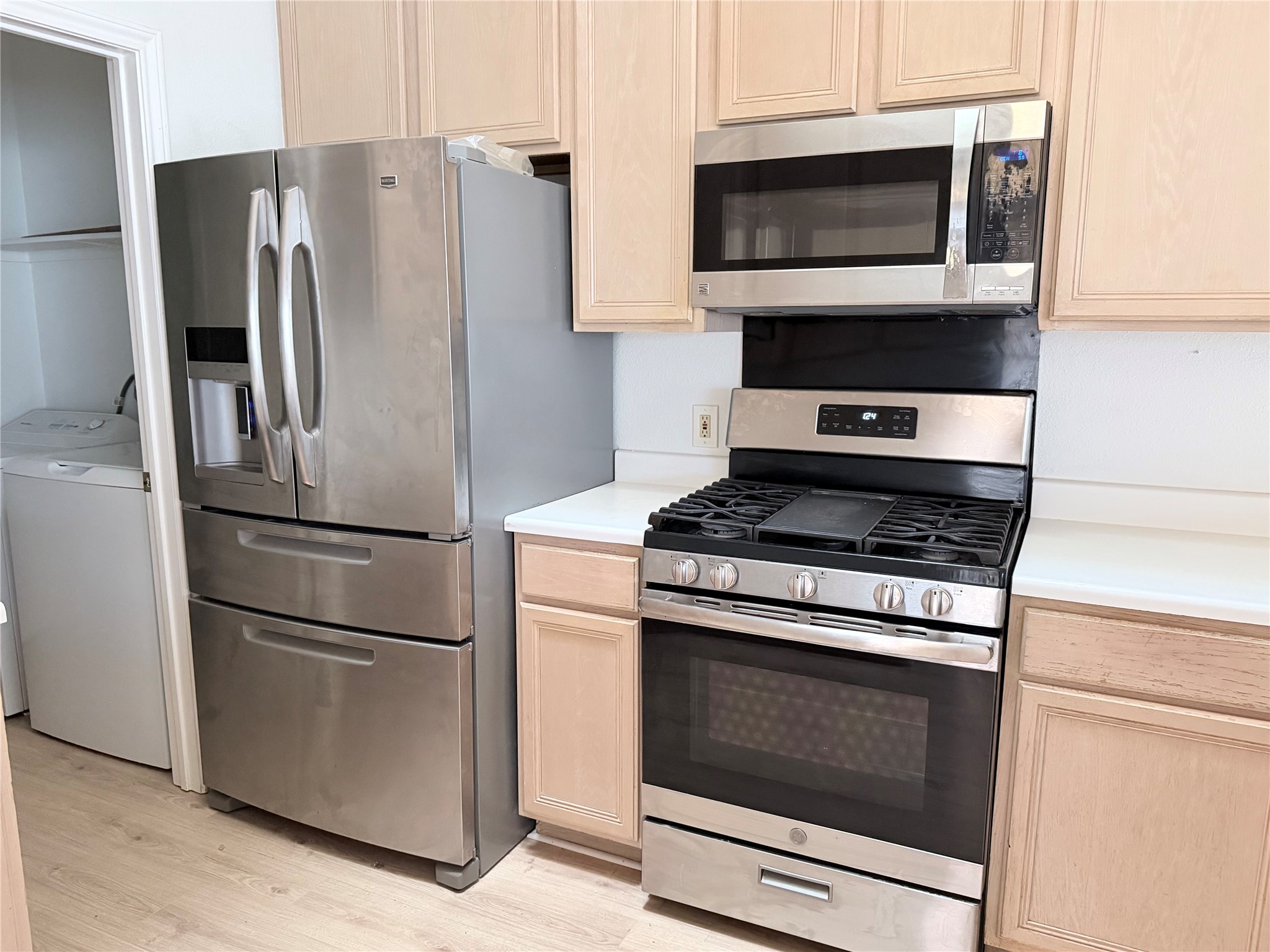 20809 Pacers Gait Lane Pflugerville, TX 78660 - Photo 22 of 23 Kitchen with stainless steel appliances, light wood finish cabinetry, light countertops, washer / clothes dryer, and light wood-style flooring