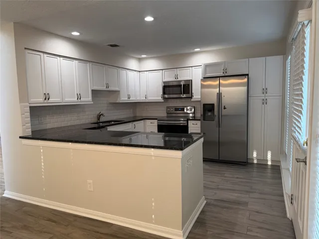 a kitchen with stainless steel appliances granite countertop a refrigerator a sink a stove a microwave and white cabinets with wooden floor