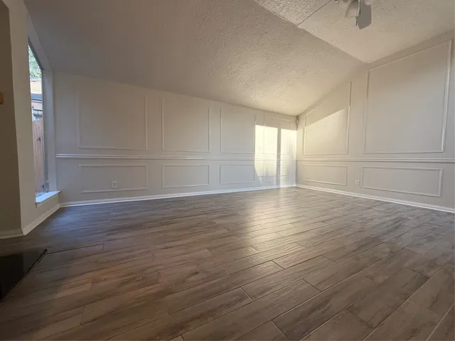 an empty room with wooden floor and windows with curtains