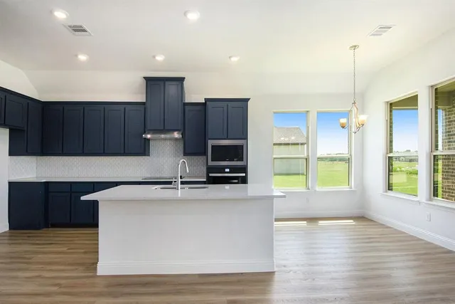 a kitchen with kitchen island granite countertop a stove top oven a sink and dishwasher with wooden floor