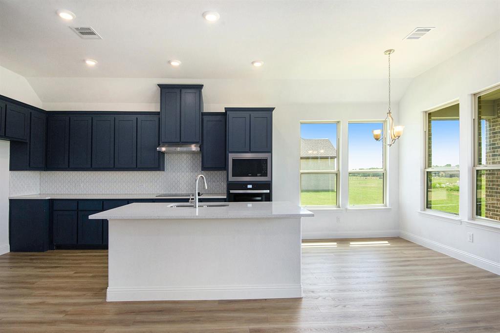 6033 Mango Drive Sanger, TX 76266 - Photo 11 of 29 a kitchen with kitchen island granite countertop a stove top oven a sink and dishwasher with wooden floor