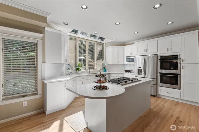 a kitchen with stainless steel appliances kitchen island granite countertop a stove a sink dishwasher and white cabinets with wooden floor