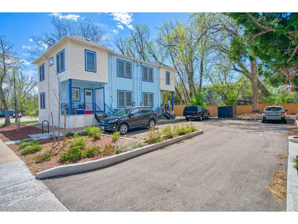 a view of a white house with a large tree and plants