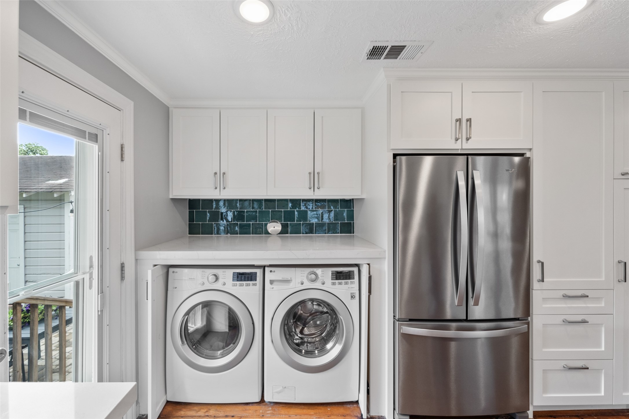 1510 Alexander Street Houston, TX 77008 - Photo 8 of 18 Full-size side-by-side washer/dryer tucked behind cabinetry with quartz counter above and matching emerald tile. Thoughtful design hiding in plain sight.