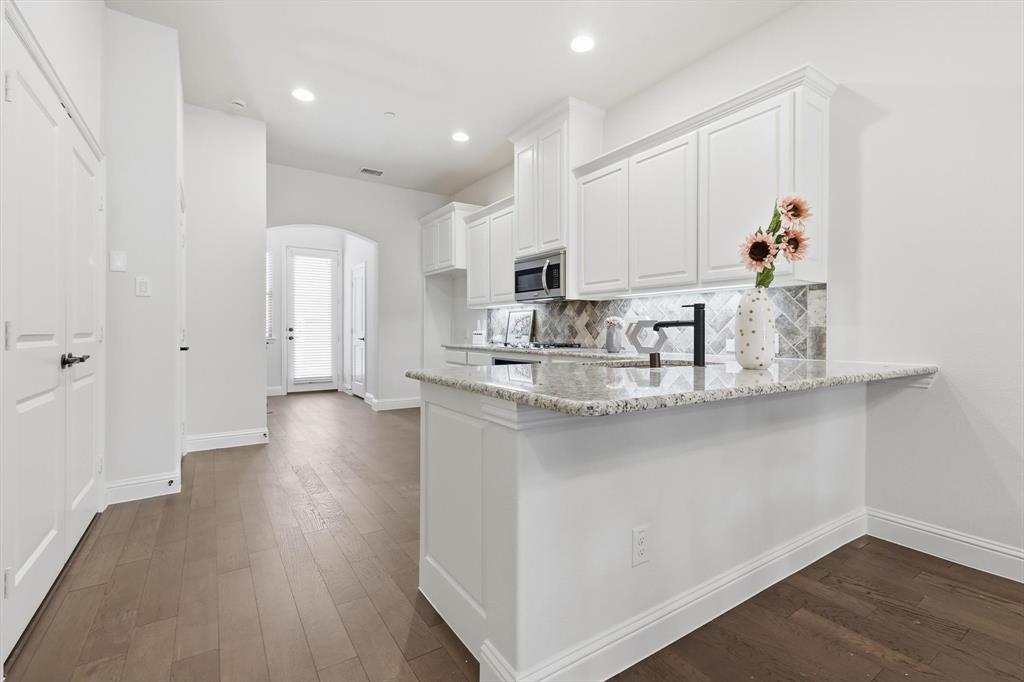 4642 Rhett Lane, Unit B Carrollton, TX 75010 - Photo 11 of 26 Kitchen featuring arched walkways, white cabinets, light stone counters, dark wood-style flooring, and tasteful backsplash