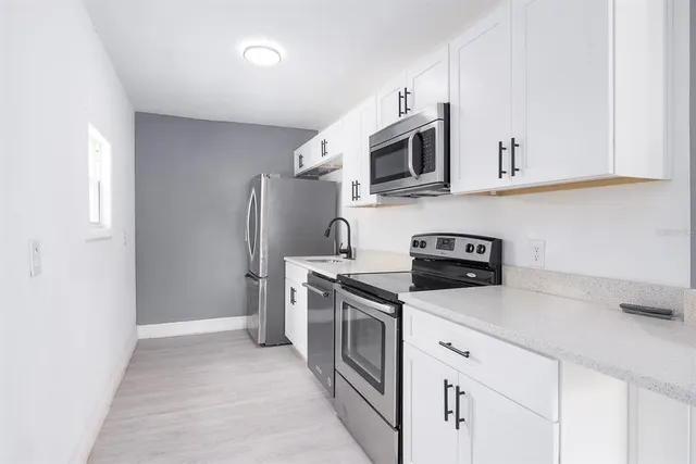 a kitchen with stainless steel appliances granite countertop white cabinets a sink a stove a refrigerator and microwave with wooden floor