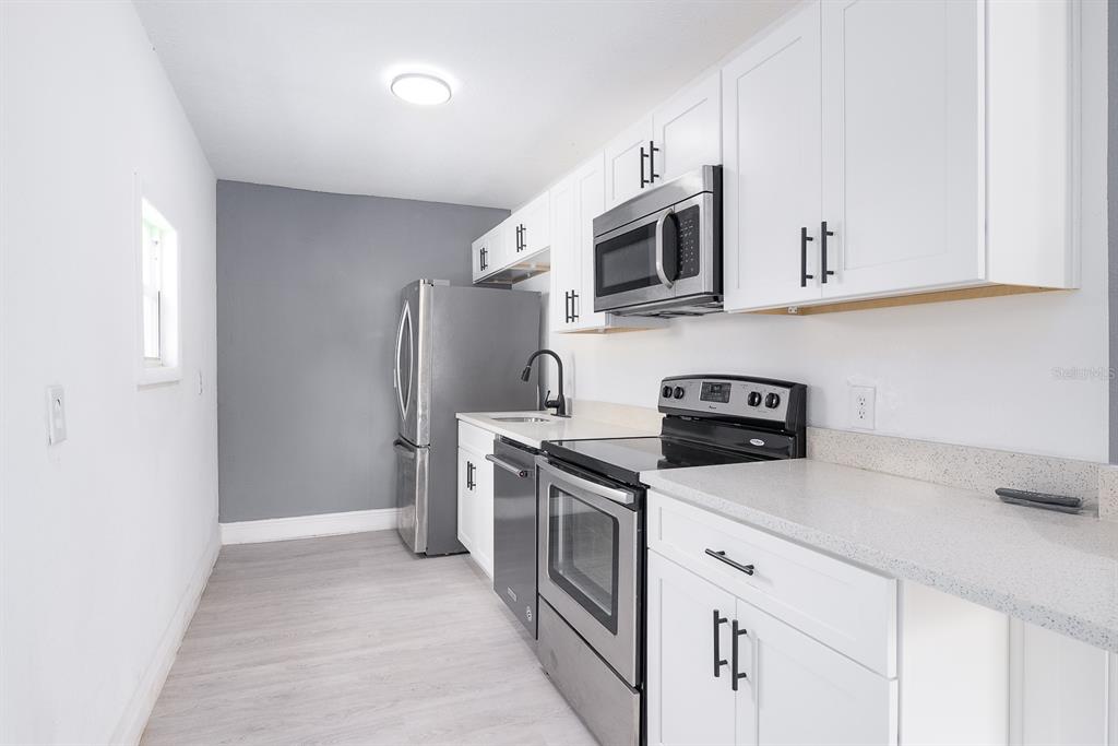 519 Williams Street Melbourne, FL 32901 - Photo 6 of 15 a kitchen with stainless steel appliances granite countertop white cabinets a sink a stove a refrigerator and microwave with wooden floor
