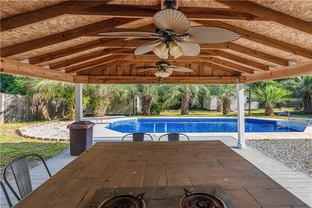 4 Ford Road Phenix City, AL 36869 - Photo 36 of 52 Wood-beam gazebo with ceiling fans and built-in cooking elements, overlooking a swimming pool with a surrounding concrete patio, and lush palm trees