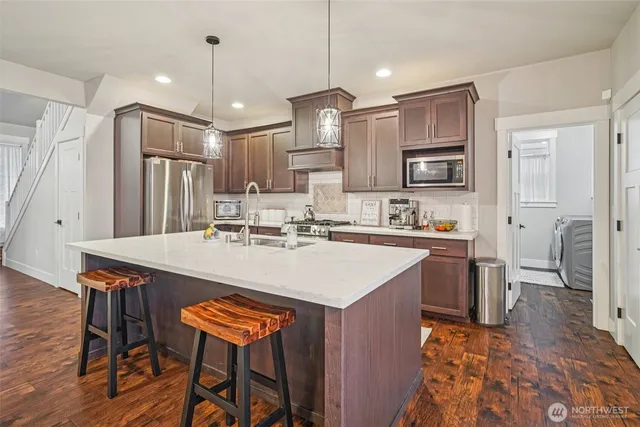 a kitchen with stainless steel appliances granite countertop a sink a stove a refrigerator and island with wooden floor